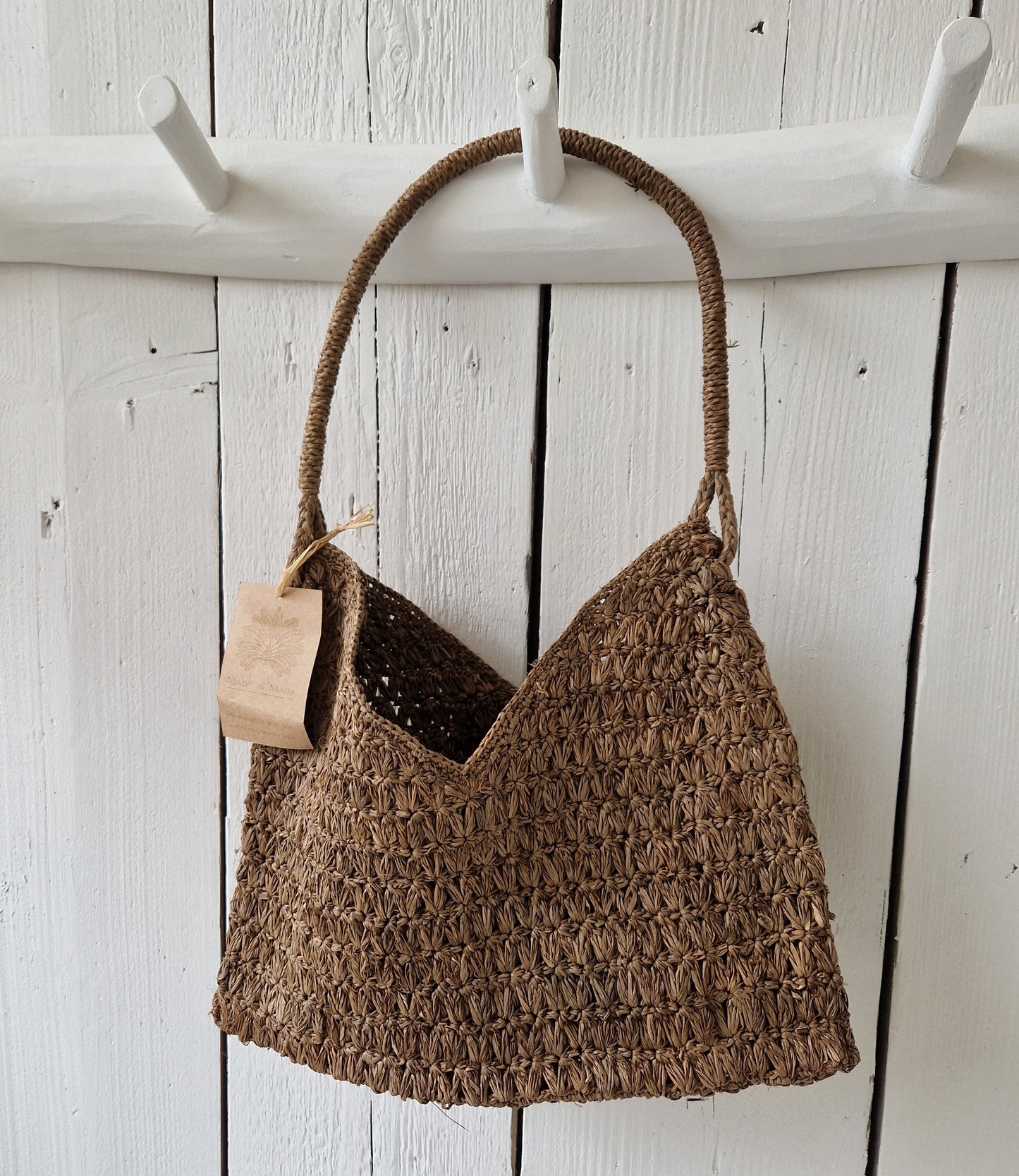 Valiha Bag van Made in Mada aan witte houten haak, handgeweven raffia tas met bohemian uitstraling en natuurlijk karakter
