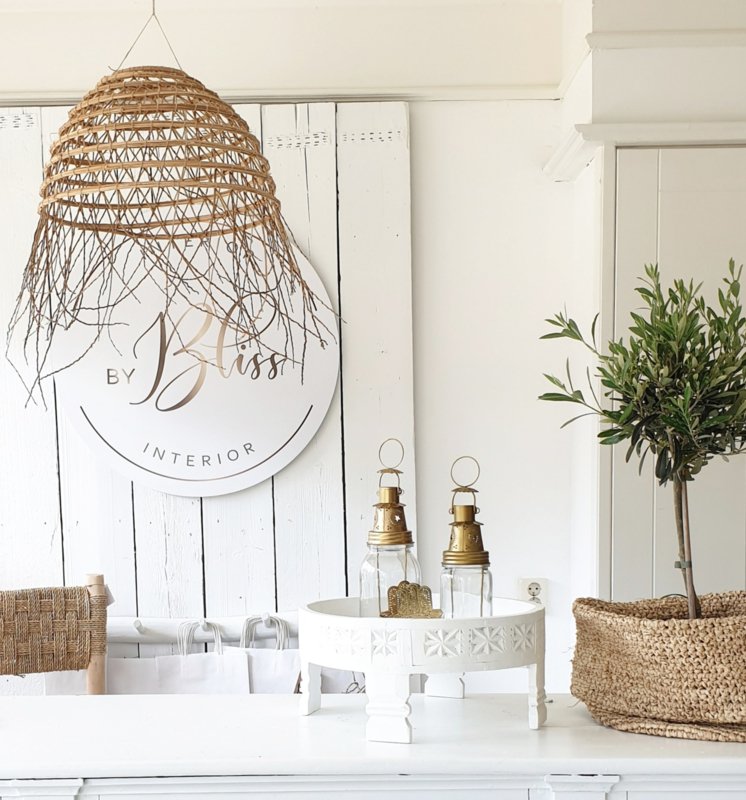 Wit interieur met wit chakki tafeltje met goudkleurige jampot lantaarntjes, daarnaast een slappe mand van palmblad met daarin een olijfboompje en daarboven een dadel hanglamp van Rock the Kasbah.