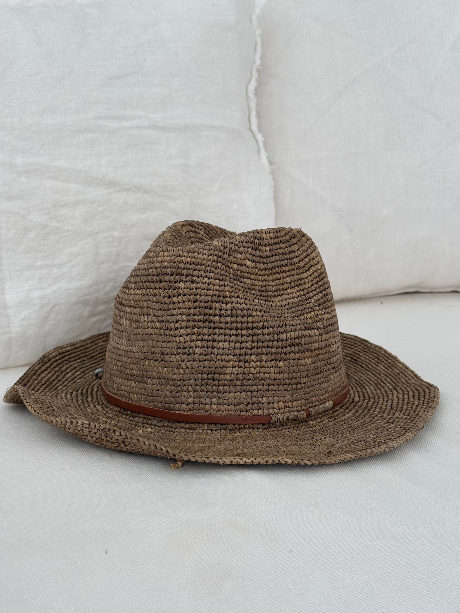 Raffia hoed Elya tan leather in tea kleur van Made in Mada op een witte linnen bank.