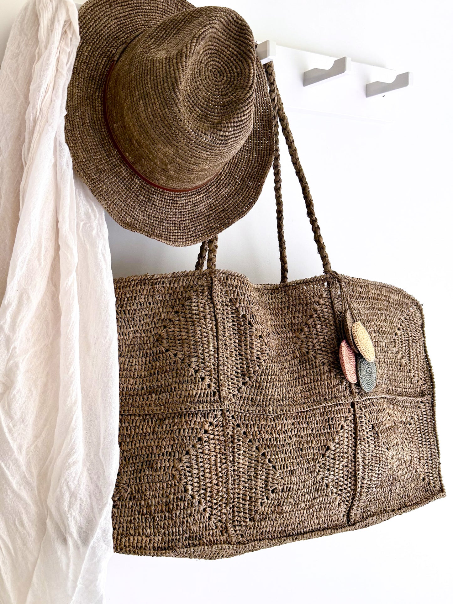 Raffia hoed Elya tan leather in tea kleur van Made in Mada aan een kapstok samen met de grote raffia Gaby bag in tea kleur van Made in Mada