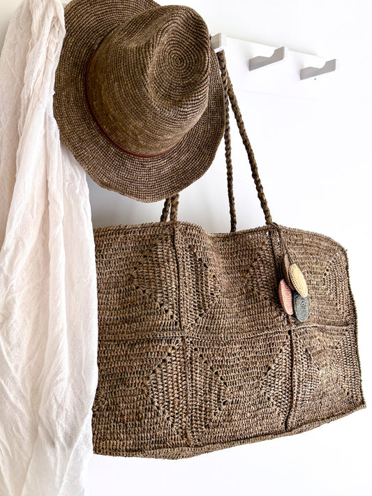 Grote Raffia tas Gabi en de Elya hat met tan leather in tea kleur van Made in Mada aan een kapstok.