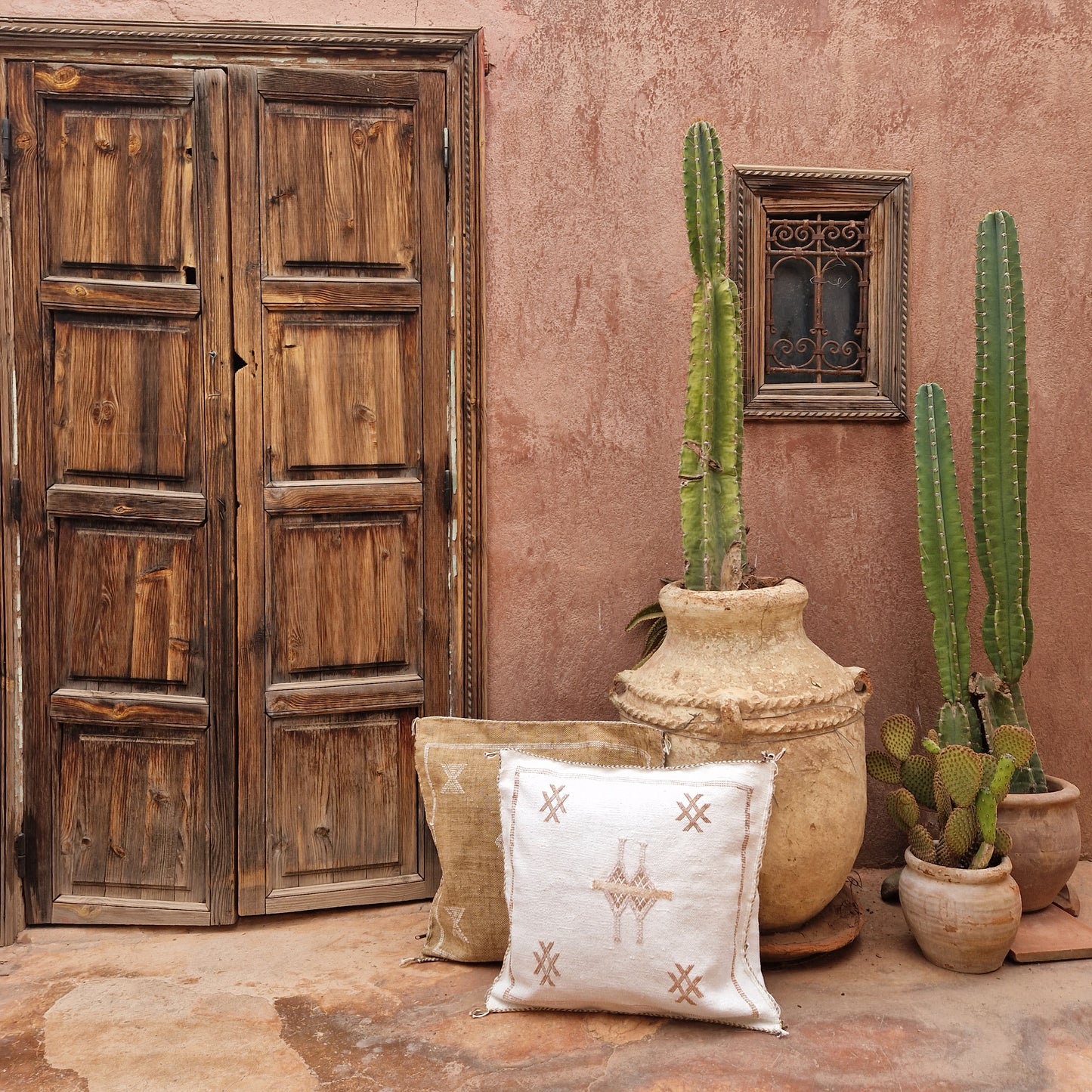 Marokkaanse kussenhoes Sabra Silk Off white en lichtbruin gestyled bij houten deur met cactus en aardewerk kruiken