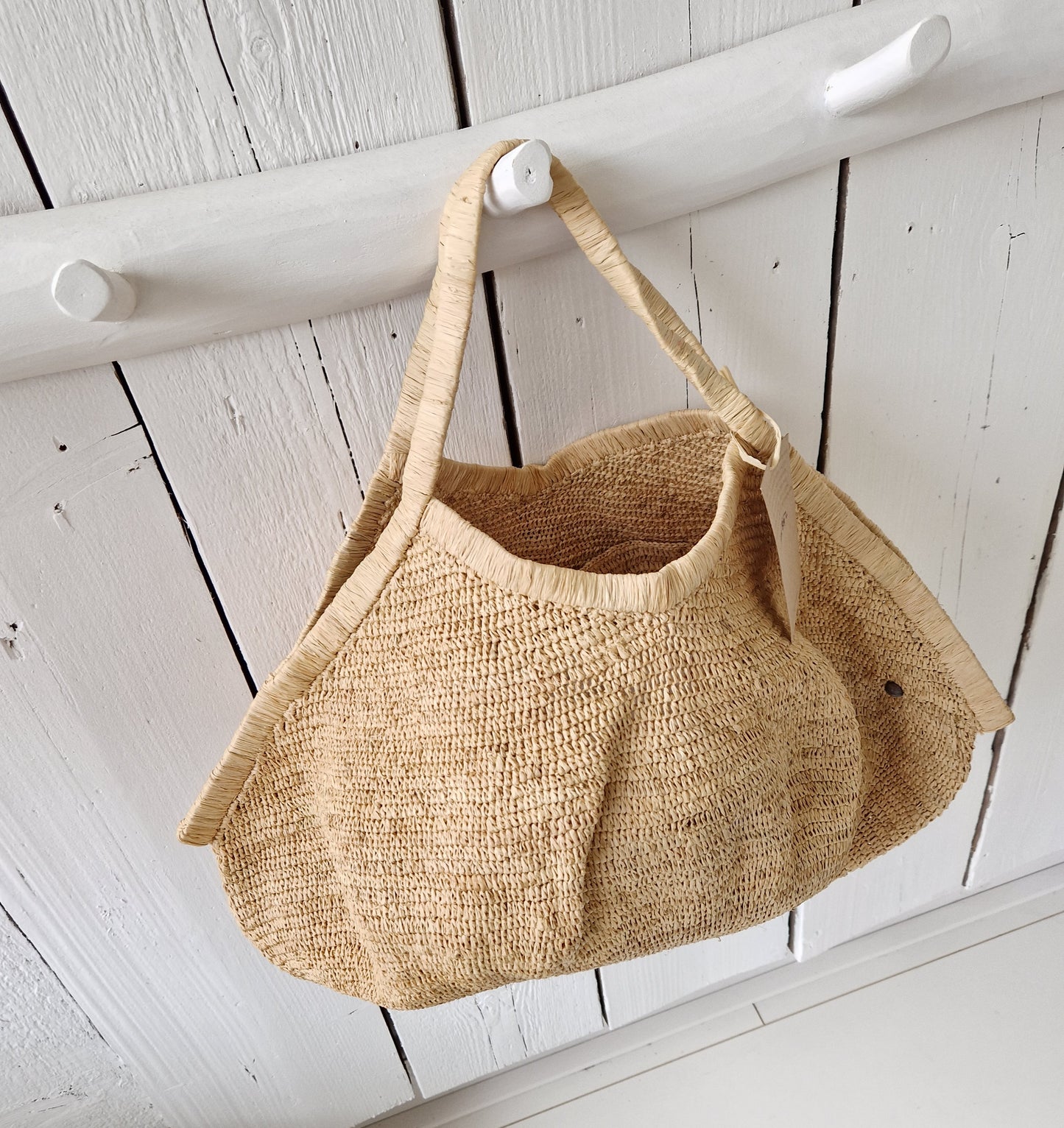 Aina Bag L Naturel van Made in Mada aan witte houten haak, handgeweven raffiatas in lichte, natuurlijke tint