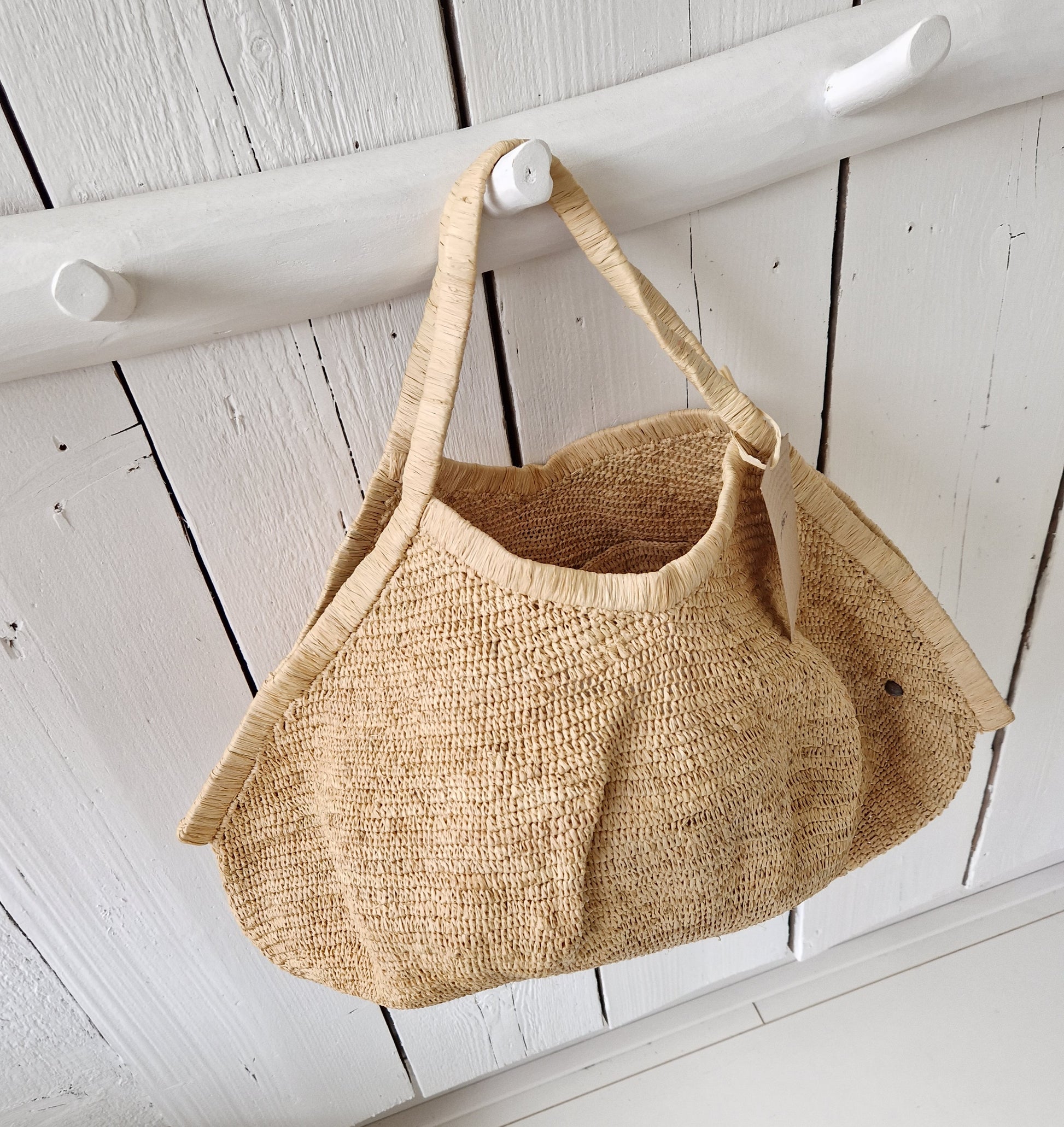 Aina Bag L Naturel van Made in Mada aan witte houten haak, handgeweven raffiatas in lichte, natuurlijke tint