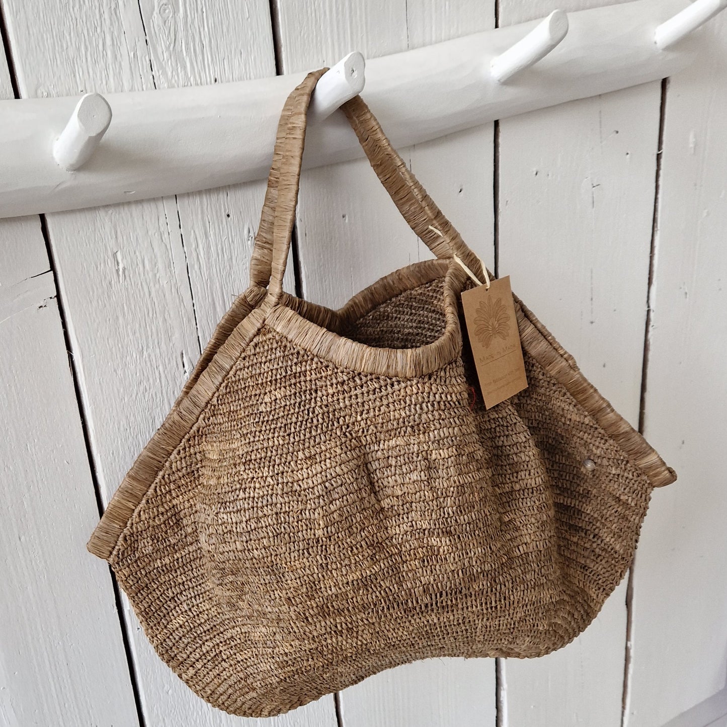 Aina Bag L Tea van Made in Mada aan witte houten haak, handgemaakte raffiatas met natuurlijke uitstraling