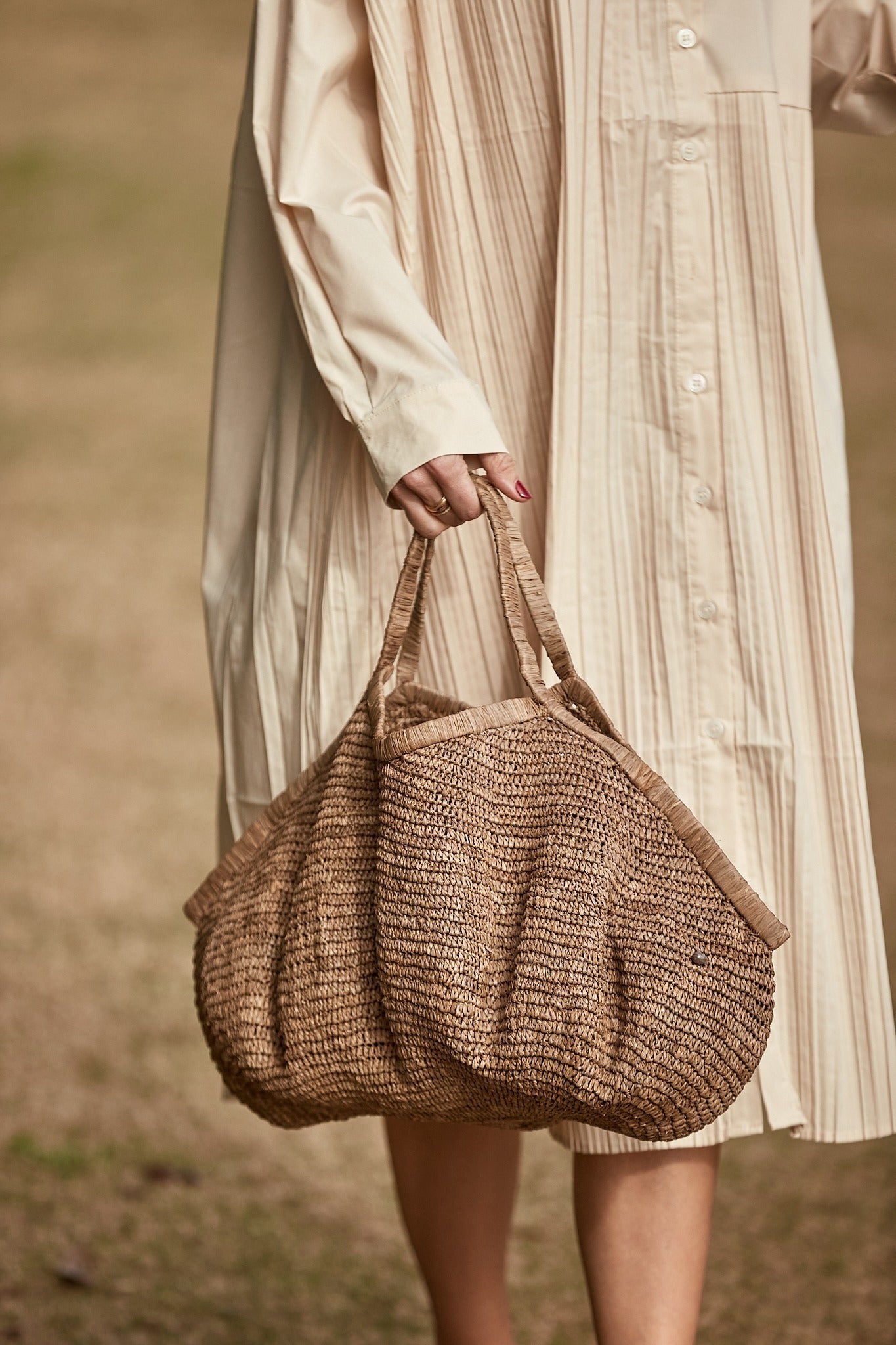 Model met de Aina Bag L Tea van Made in Mada in de hand, natuurlijke raffiatas als stijlvol accessoire bij een lichte jurk
