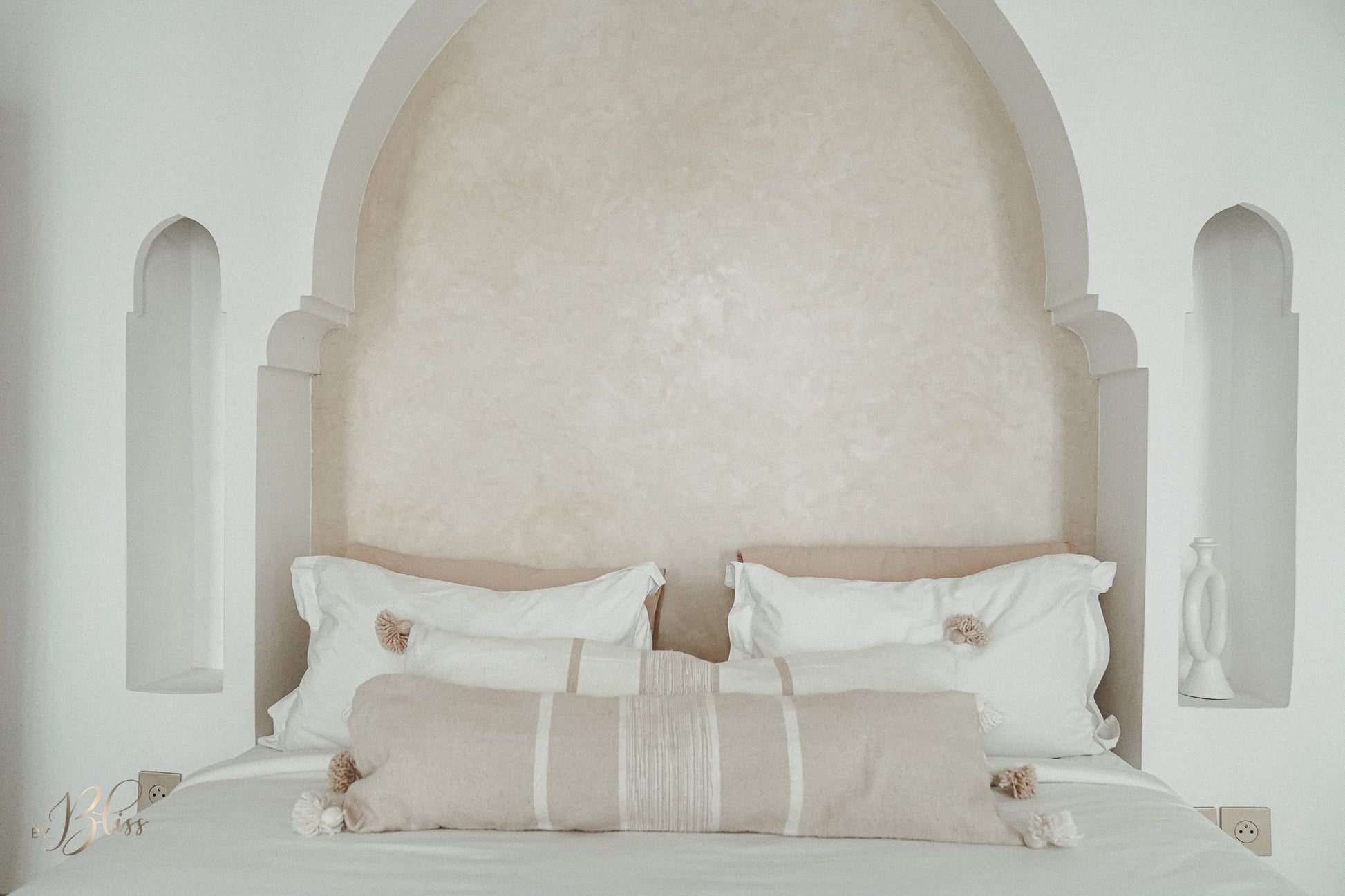 Marokkaanse pompom kussens beige en off-white in langwerpig formaat 30x100 op bed in een riad met een warm licht interieur